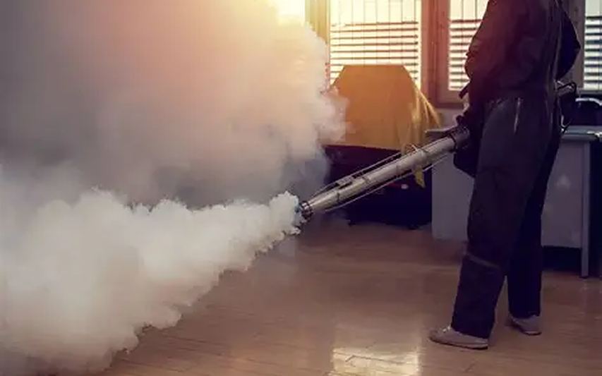 Técnico a aplicar termonebulização num interior, com fato de protecção