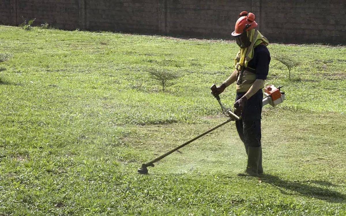 Profissional a cortar relva com roçadora, equipado com capacete e protecção