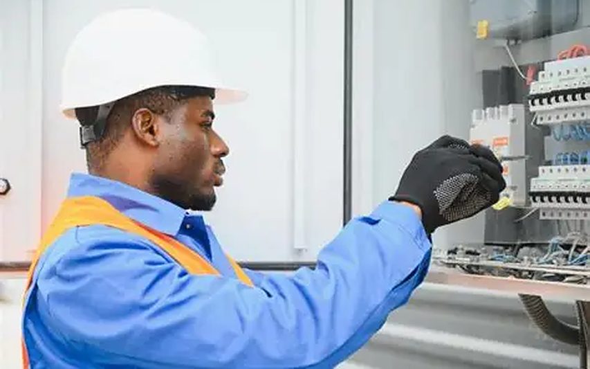 Técnico a intervir num quadro eléctrico, com capacete e luvas de protecção